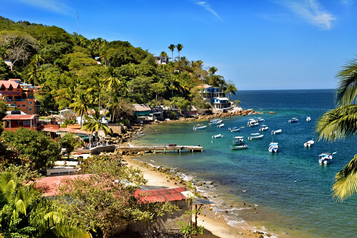 Playa mexicana tranquila con barcas y pueblo costero auténtico al fondo