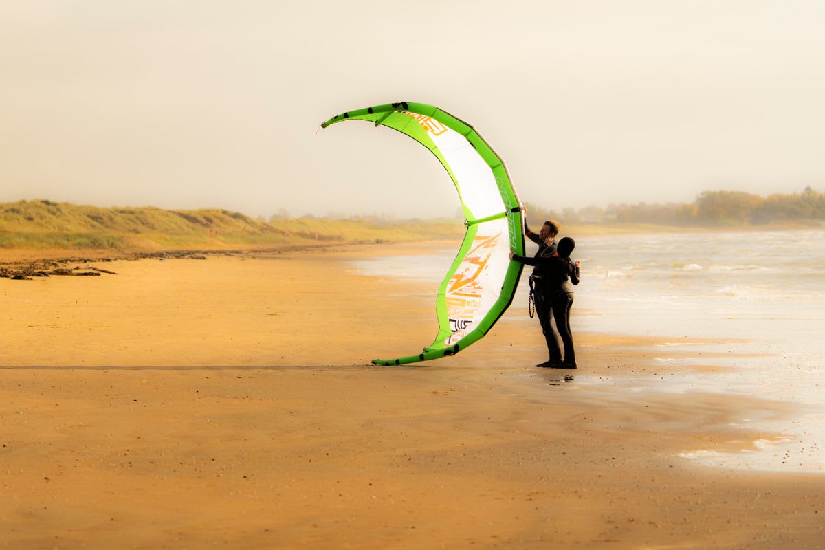 Two kitesurfers preparing their kite equipment on the beach during a golden sunset