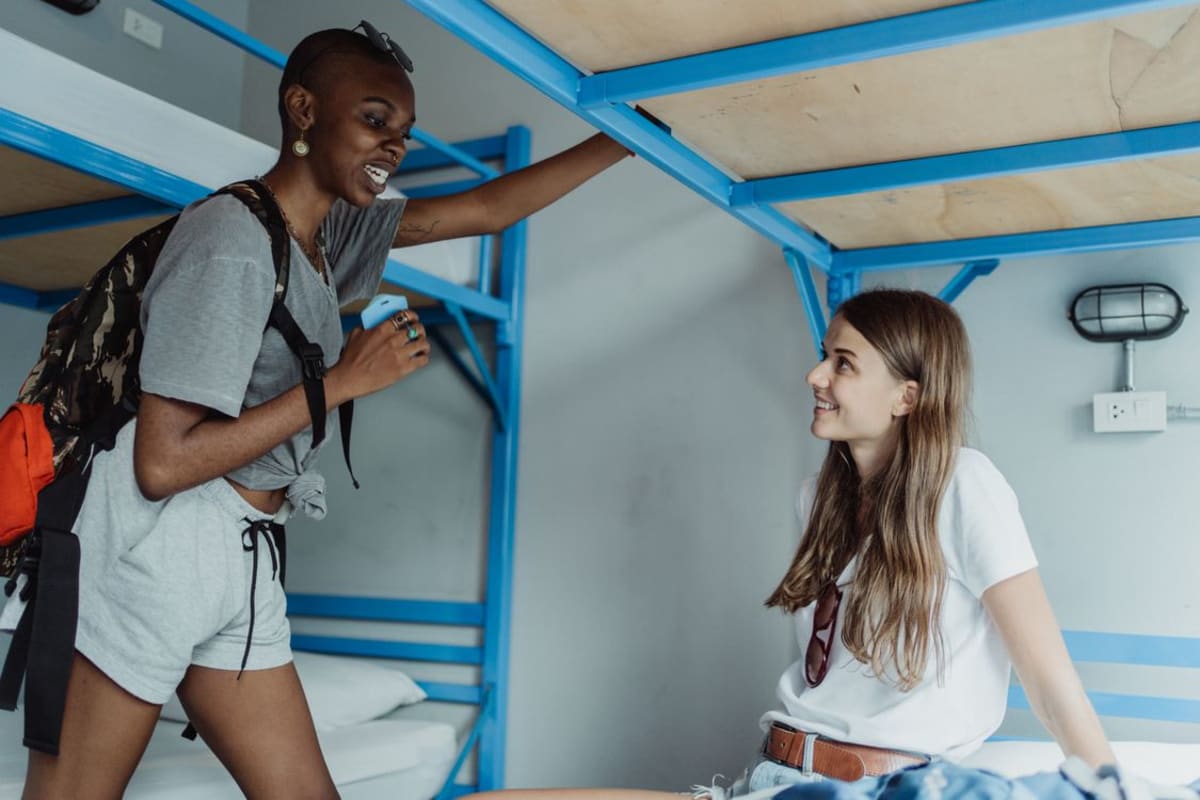Travelers socializing and talking in a hostel common room with bunk beds in the background
