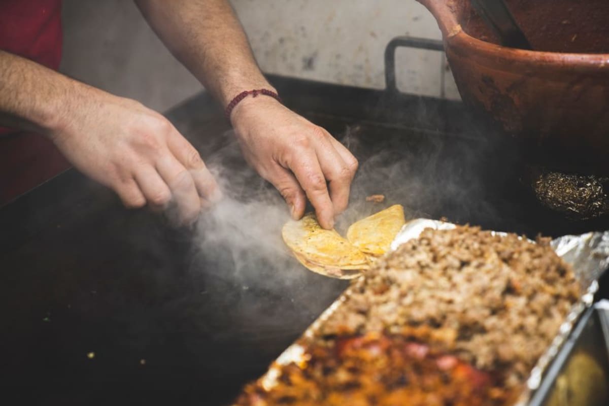 Spanish phrases for ordering food in Puerto Escondido — street taco vendor skillfully preparing authentic Mexican tacos on a sizzling grill