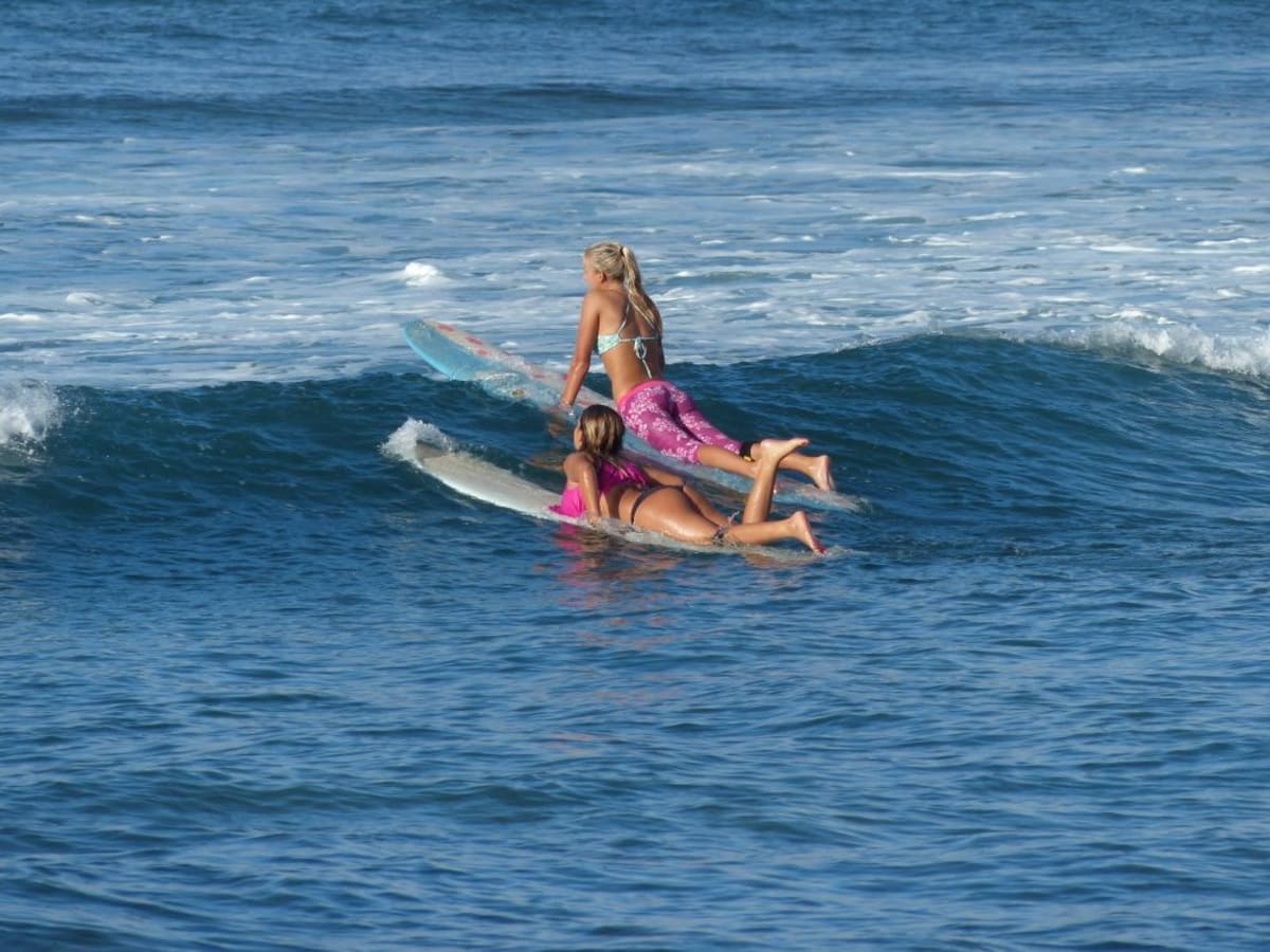 Frau lernt Surfen auf einer tropischen Welle und paddelt in den Ozean