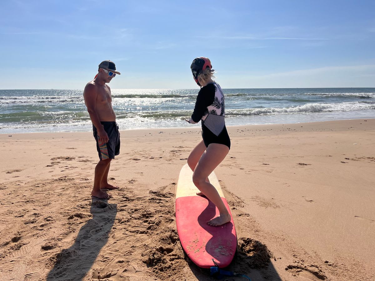Surf instructor teaching a student in shallow tropical beach water with proper technique