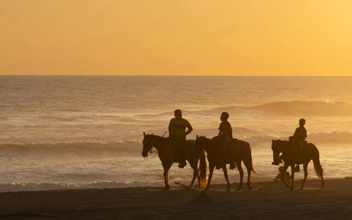 Horseback riders silhouetted against a vivid Pacific sunset on the beach near Puerto Escondido