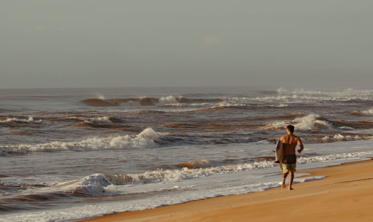 Surfer carrying a board along the sunny shore of Puerto Escondido, Mexico in January