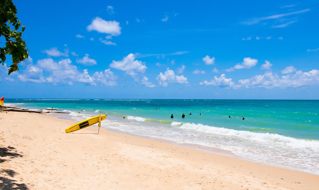 Yellow surfboard resting on a tropical beach with turquoise waters under clear January skies in Puerto Escondido, Mexico