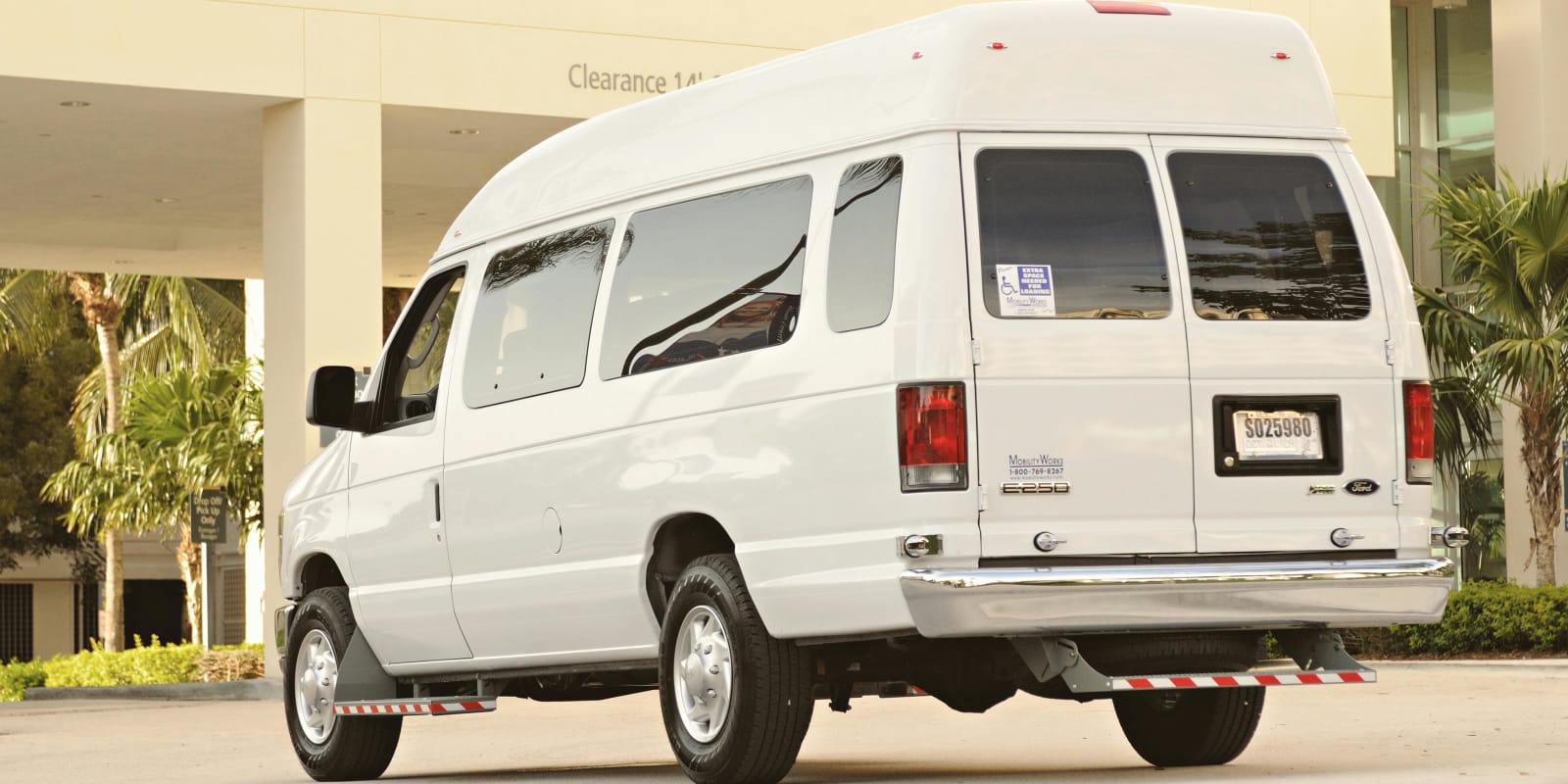 White passenger van parked outside a building with palm trees, ready for a transfer