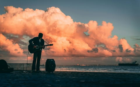 Silhouette of a guitarist playing live music by the Pacific Ocean at sunset in Puerto Escondido Mexico