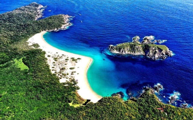 Aerial view of a curved white-sand beach and a turquoise bay framed by green hills in Huatulco