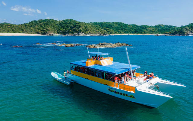 A boat crossing a deep blue bay framed by jungle in Huatulco