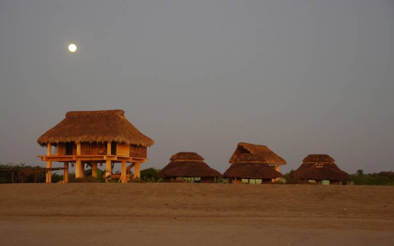 Rustic palapa cabanas at dusk with the moon rising over Chacahua beach