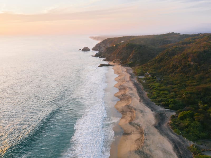 Aerial view of the Oaxaca coastline with dramatic cliffs and surf at sunset