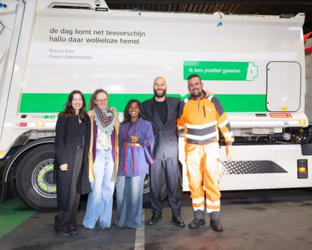 Three women and two men pose beside a rubbish truck which has two lines of poetry emblazoned on its side.