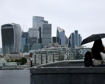 A woman holds a black umbrella in view of the City of London skyline