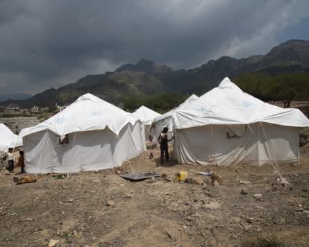 People stood next to white canvas tents set up in an empty bit of land