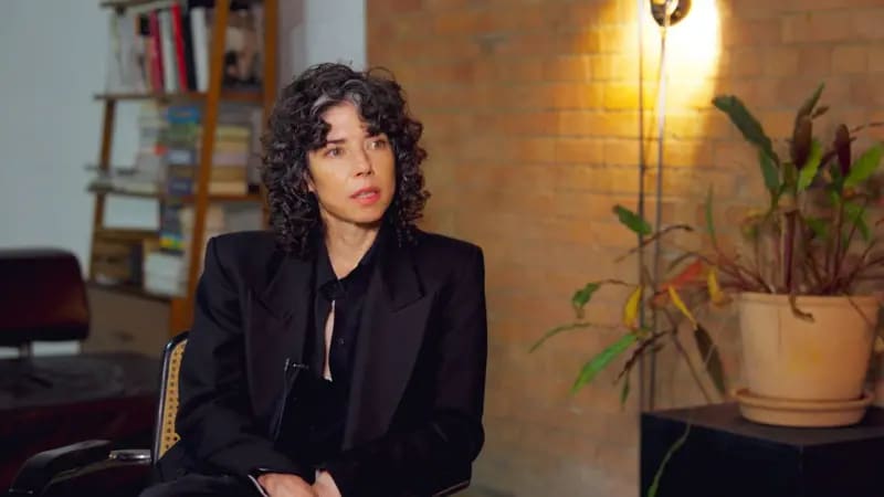 Meredith Whittaker sentada, siendo entrevistada. Viste una blusa y una chaqueta negras y tiene el pelo oscuro y rizado. Está en el interior de una vivienda. Detrás de ella se ve una pared de ladrillo 