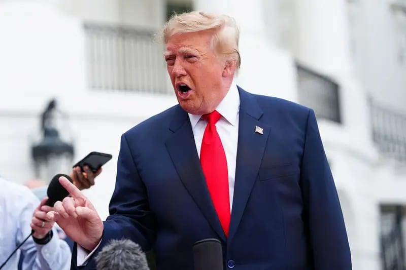 El presidente Trump habla y gesticula ante los reporteros. Viste chaqueta oscura y corbata roja.