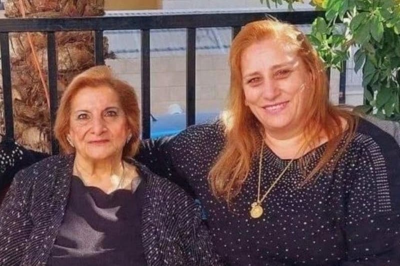 Nahida y Samar Anton están sentadas sonriendo una al lado de la otra frente a una barandilla. Ambas llevan blusas negras con pequeños lunares blancos, mientras que Samar luce una cadena de oro con un