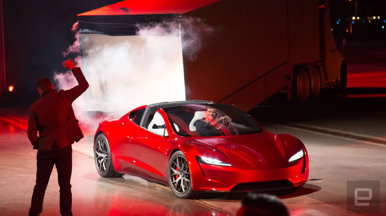 A Tesla Roadster on a stage with Elon Musk pumping his fist in front of it. Image from 2017.