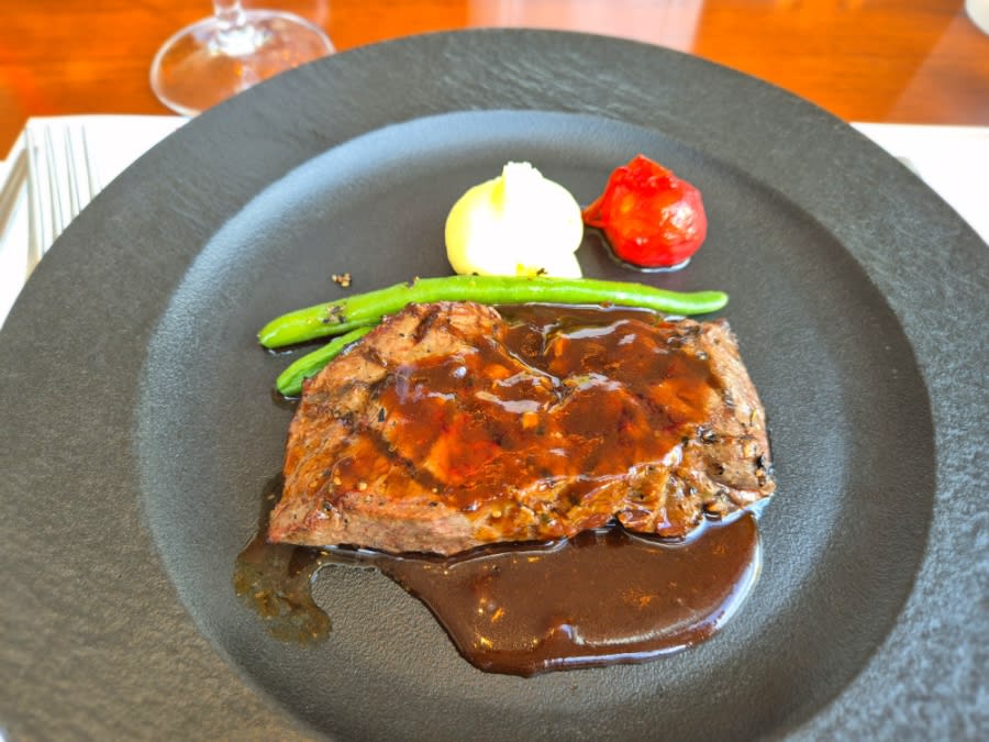 Flat iron steak with sauce, green beans, mashed potato and a roasted tomato on a dark plate