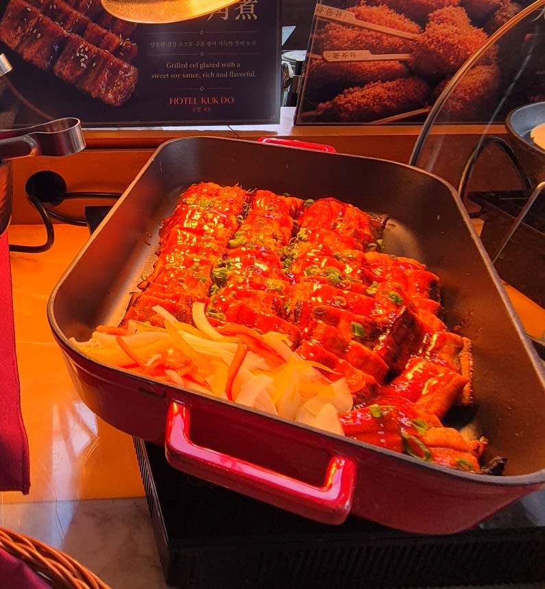 Red tray of glazed grilled eel pieces with sliced onion and scallion