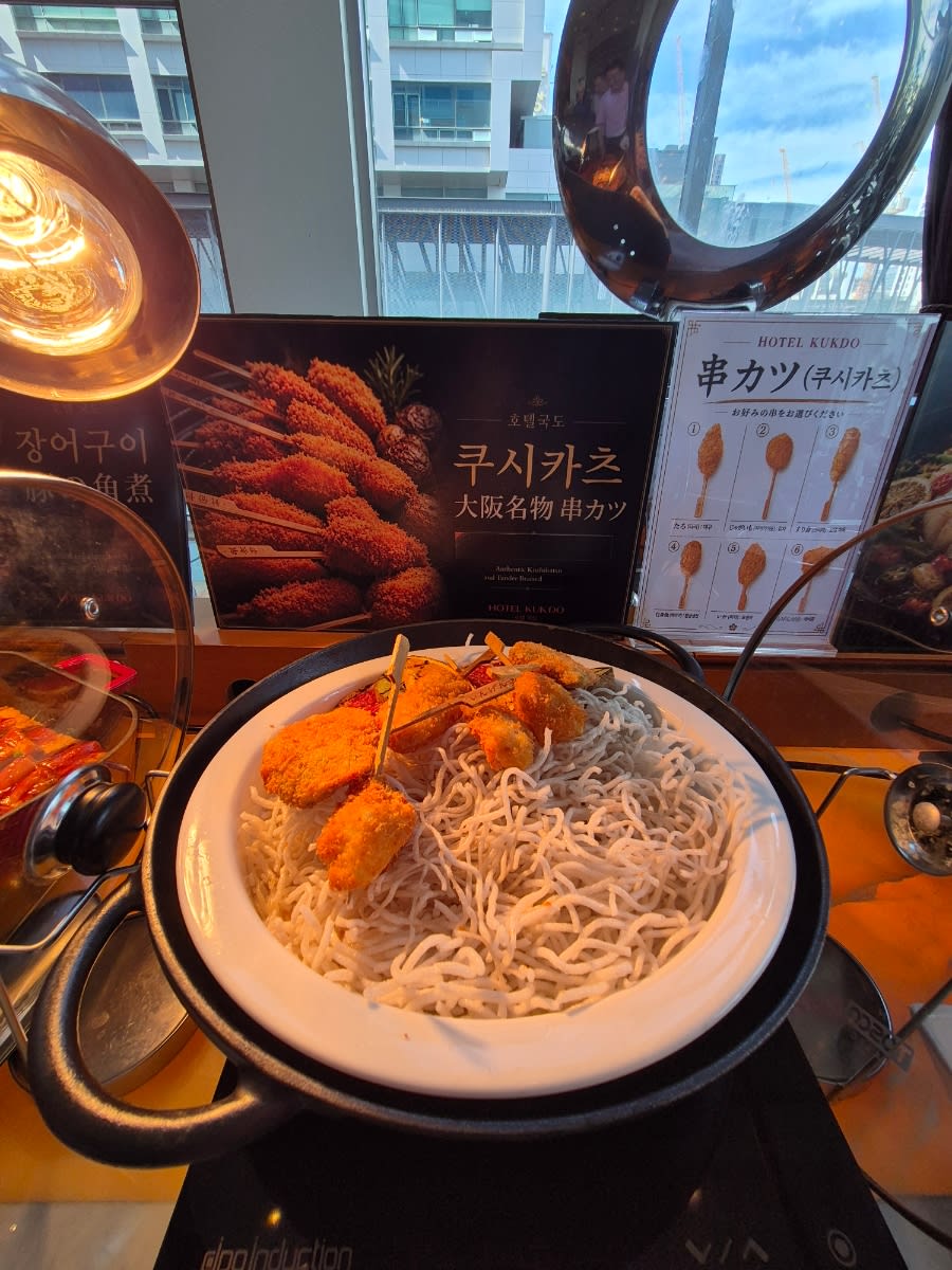 Fried kushikatsu pieces on skewers in a white bowl at a hot buffet station