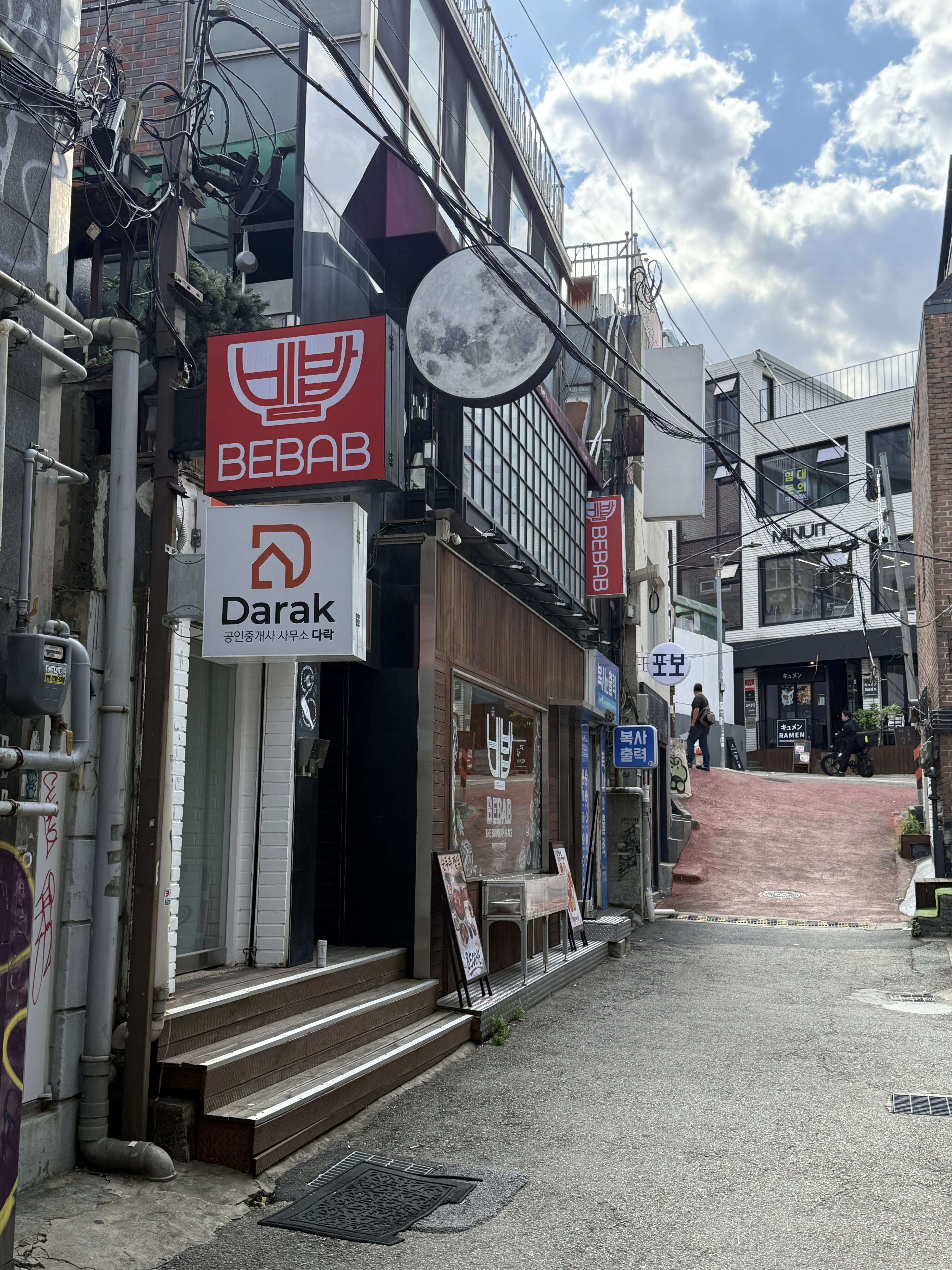 A narrow alley leading to Bebab, with a red BEBAB sign and a round moon-shaped sign above the entrance