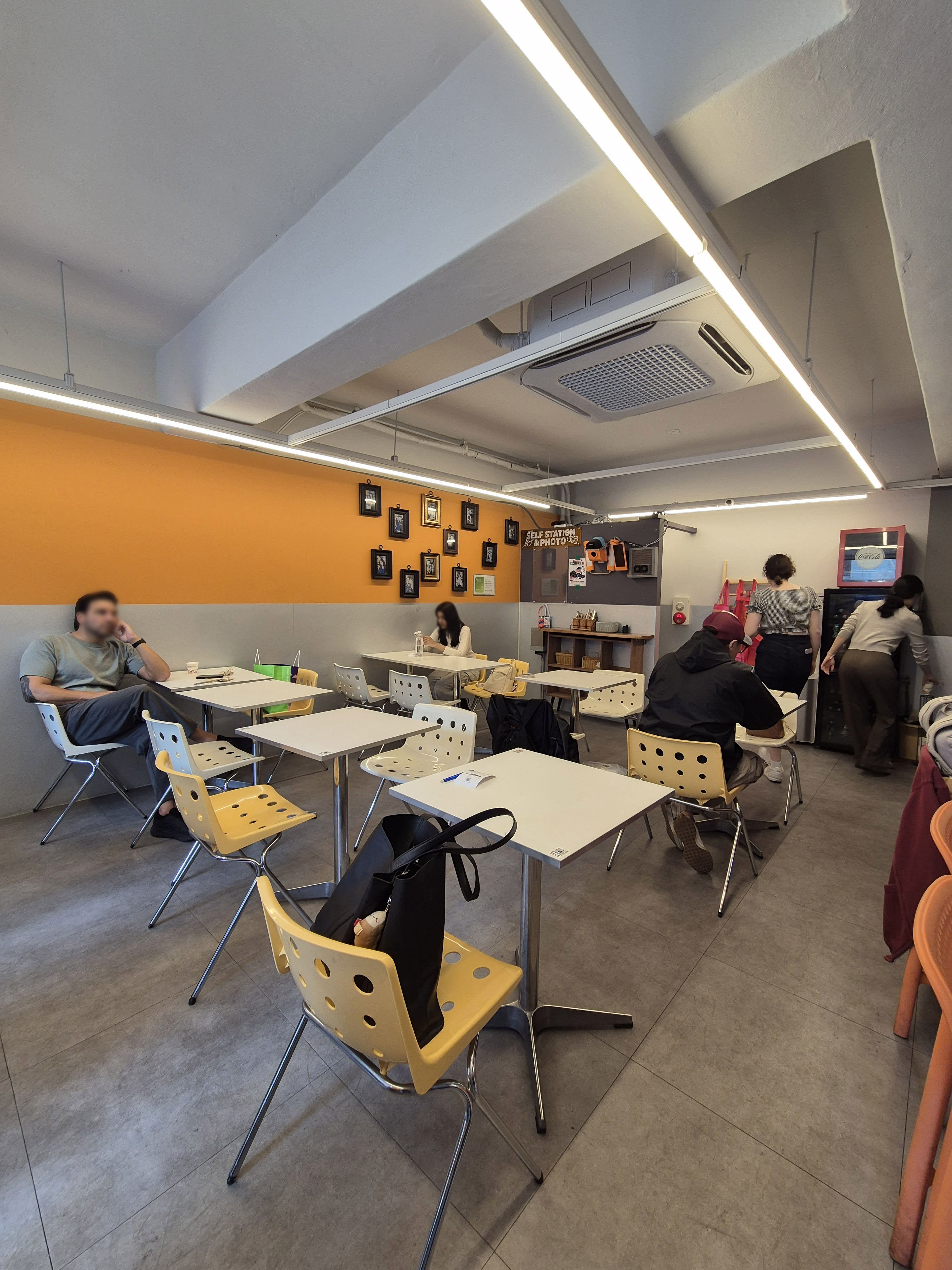 Bebab's dining room with an orange accent wall, small framed pictures, and white tables with yellow perforated chairs