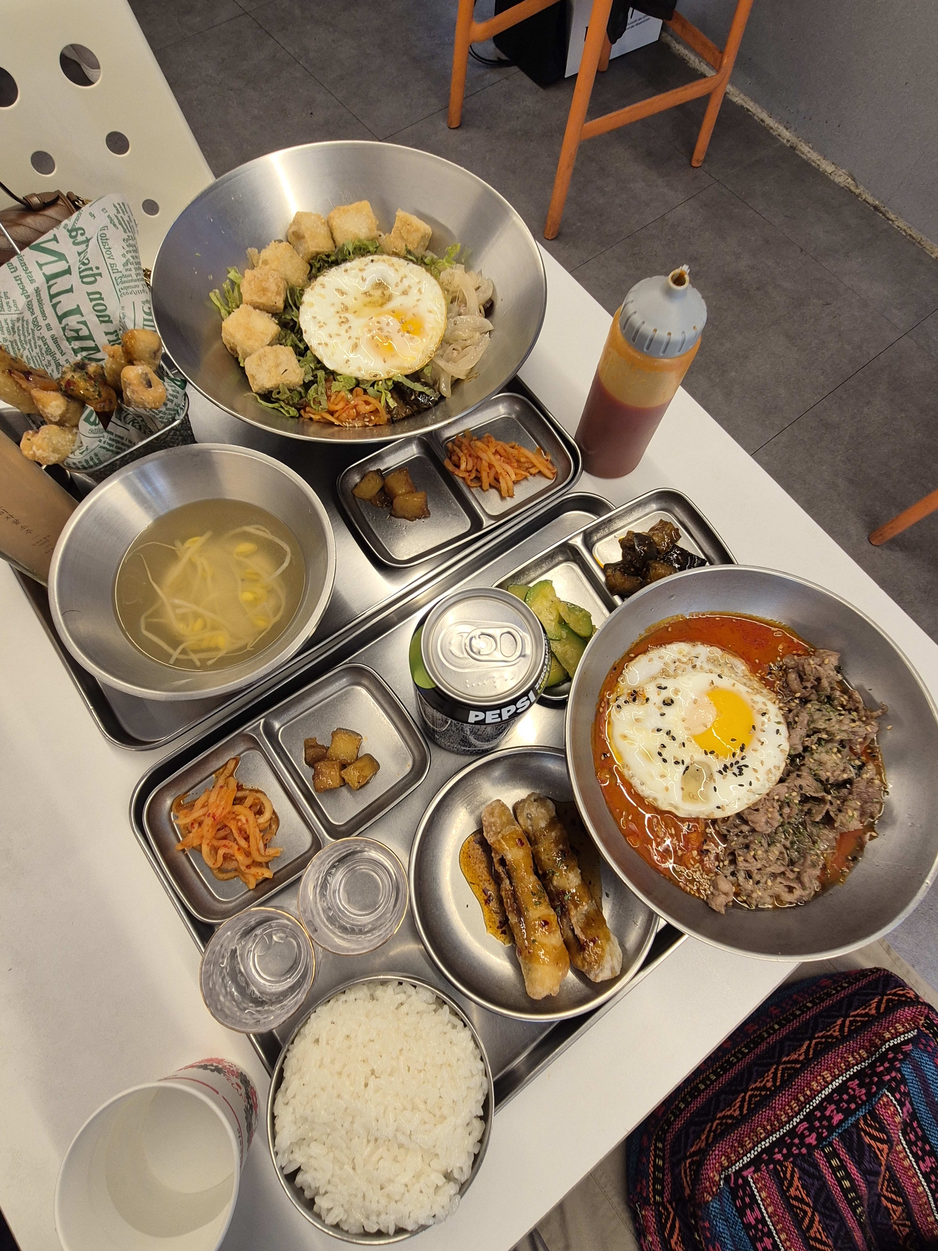 A full view of the table spread with both bowls, side dishes, soup, rice, the soju bottle and a Pepsi can