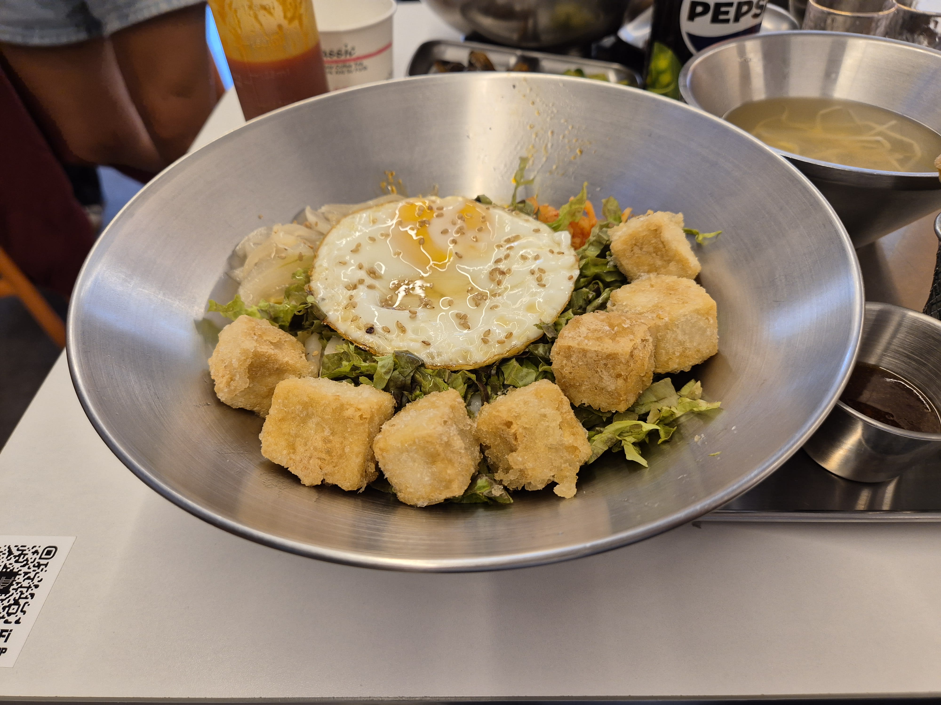 Dubu gyeran bibimbap in a metal bowl with a fried egg, fried tofu cubes and shredded lettuce