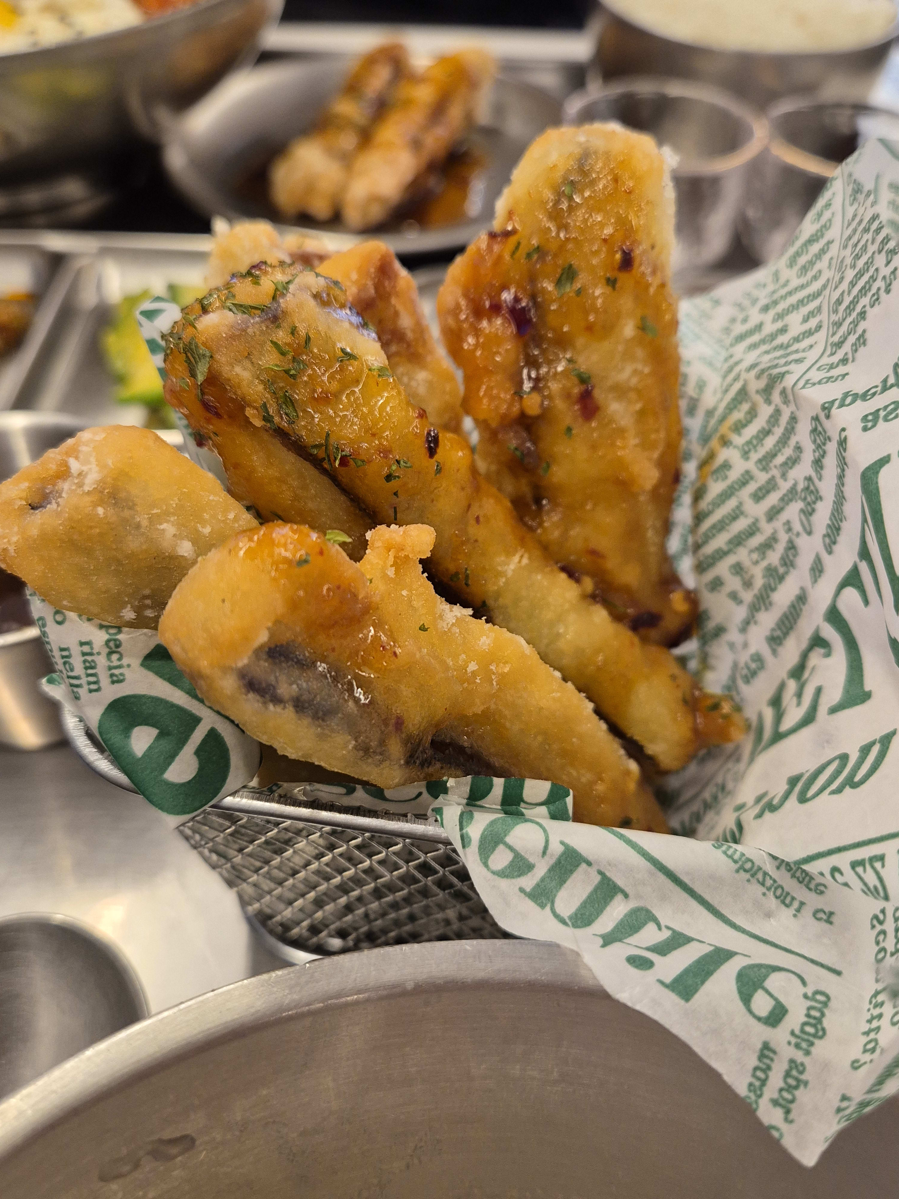 Kkanpung gaji in a paper-lined metal basket, fried pieces sprinkled with herbs and what looks like chili flakes