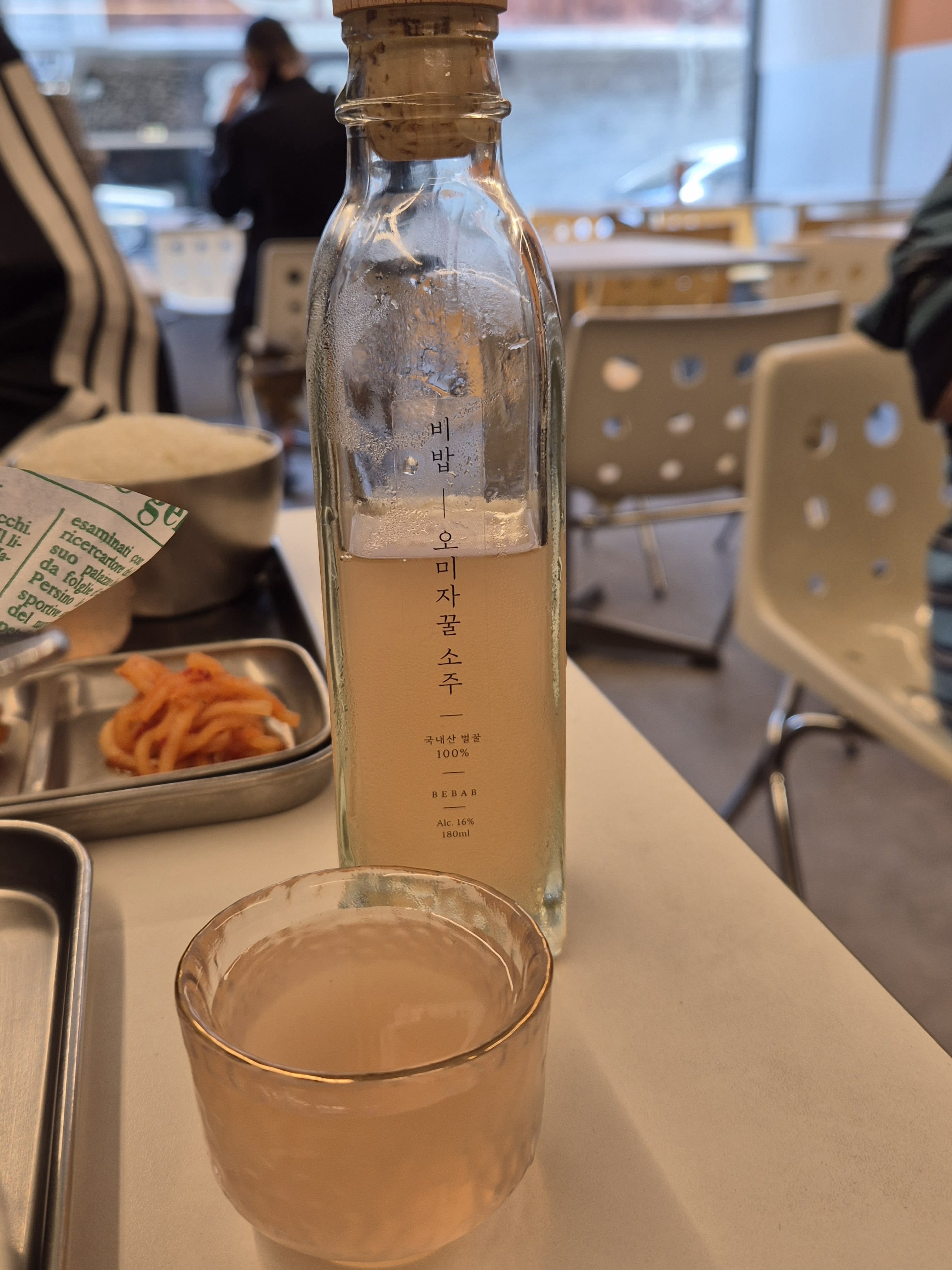 A bottle of omija kkul soju labeled Bebab, 180ml, next to a filled glass
