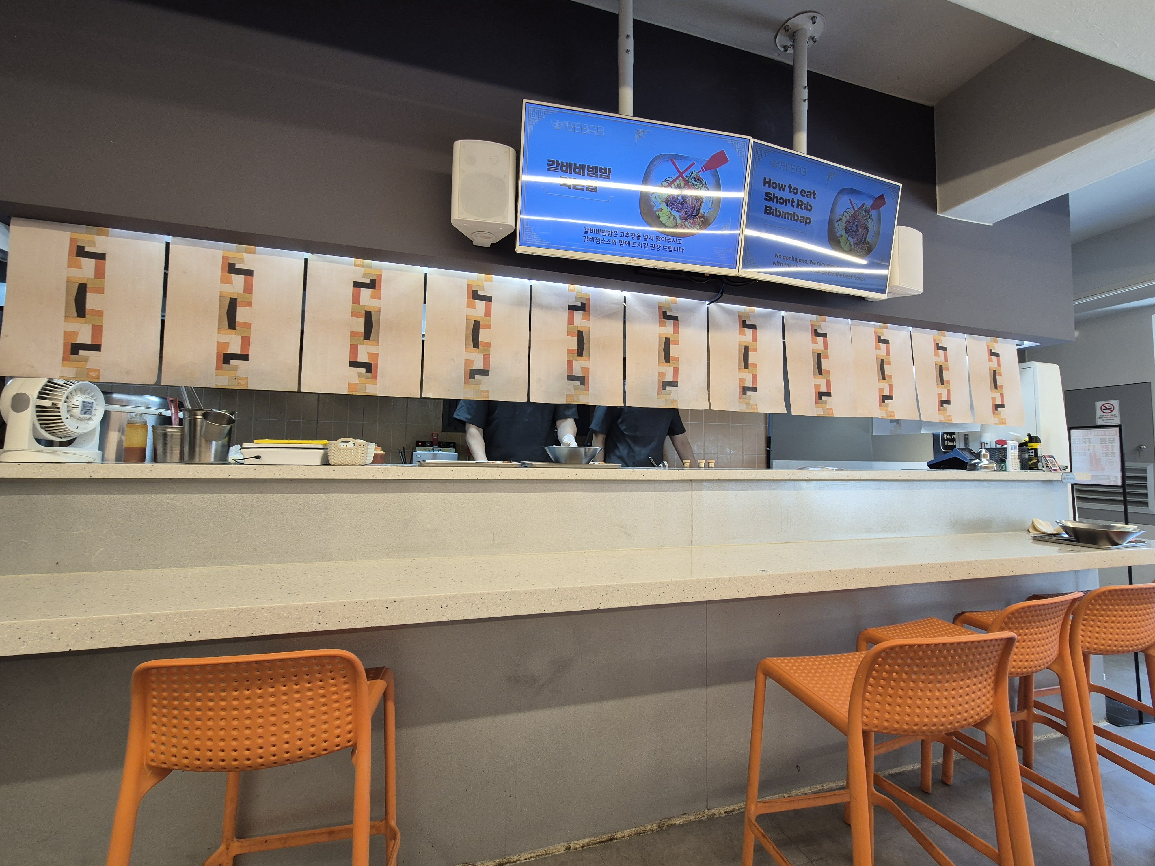 The open kitchen pass-through at Bebab with a row of orange bar stools facing it