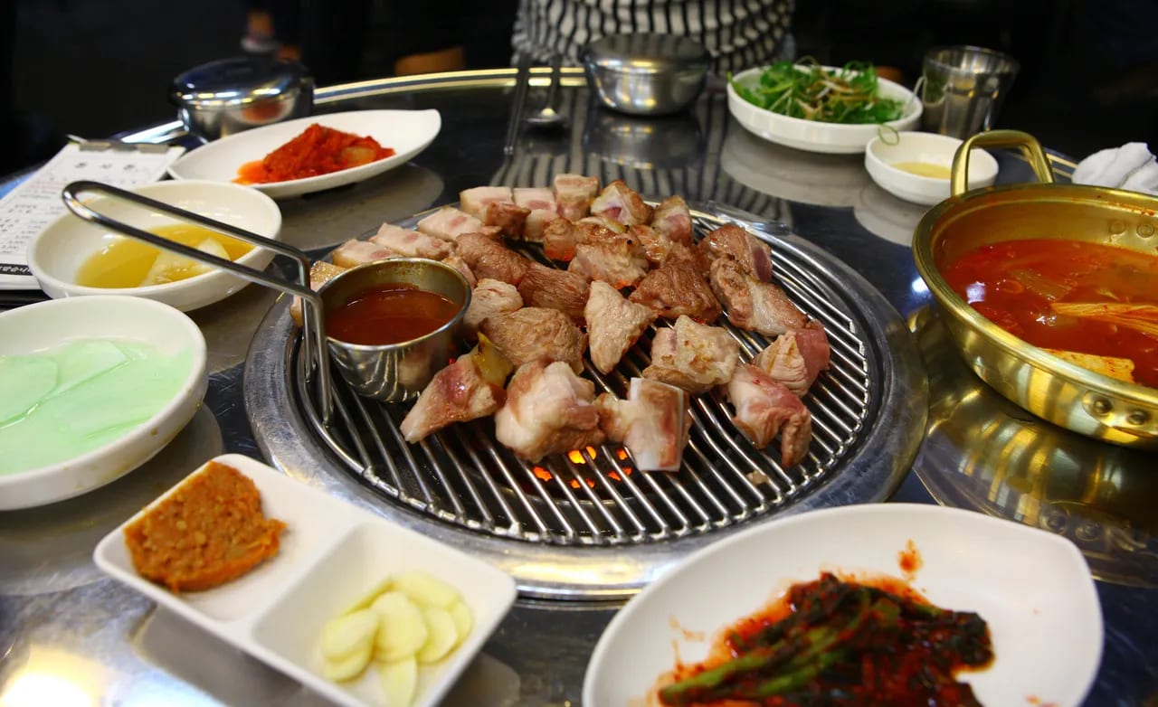 Authentic Korean BBQ table setting with grilling meat, fresh lettuce for Ssam, and various side dishes in Seoul.