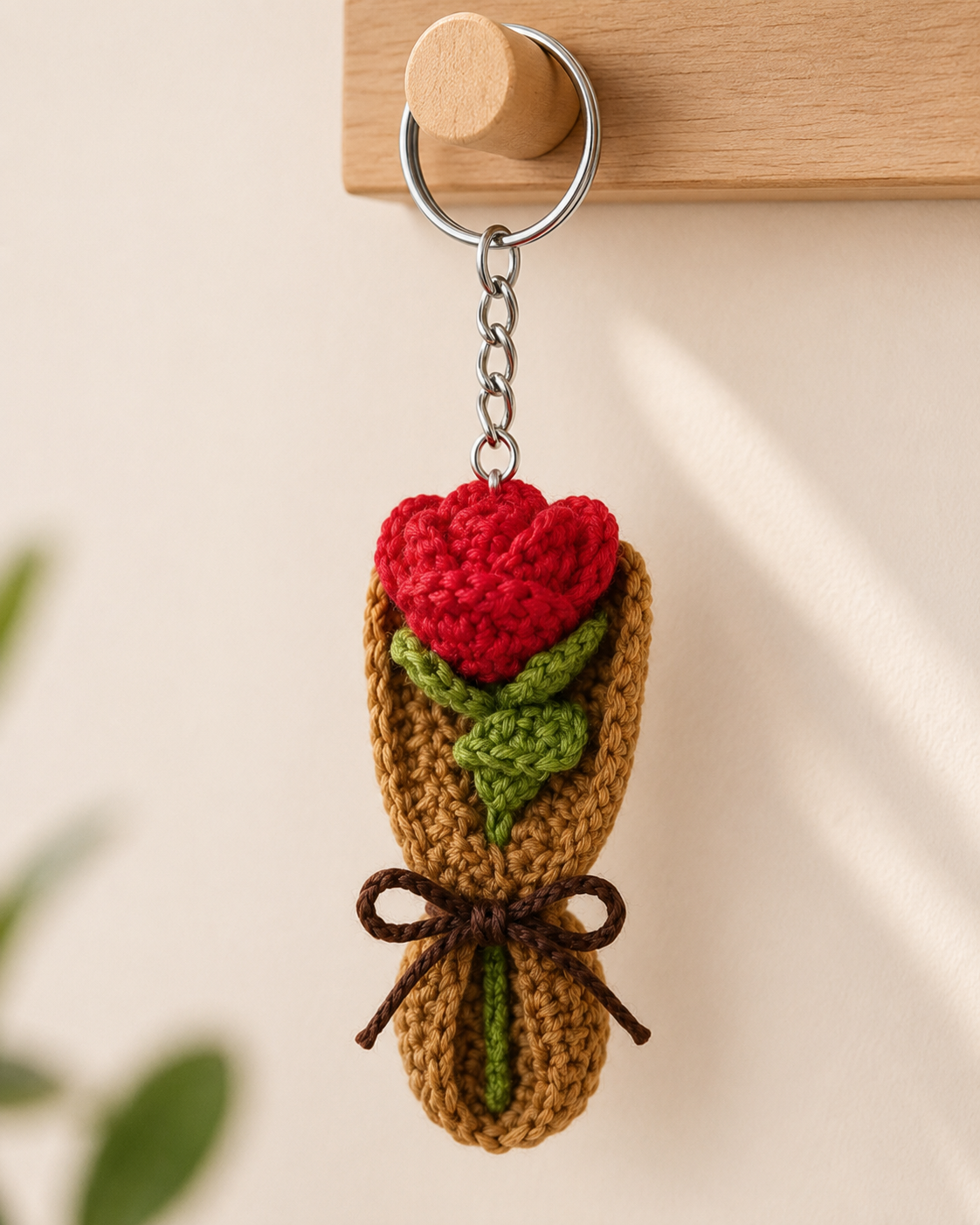 Rose Bouquet Keychain hanging on a wooden wall hook, red rose charm with green leaves, brown bouquet wrap and metal keyring.
