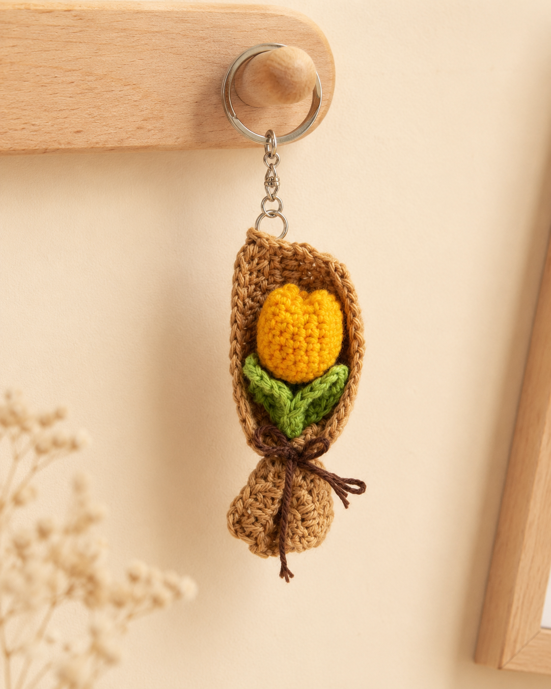 Yellow Tulip Bouquet Keychain hanging on a wooden wall hook, handmade crochet flower charm with brown wrap and metal keyring.