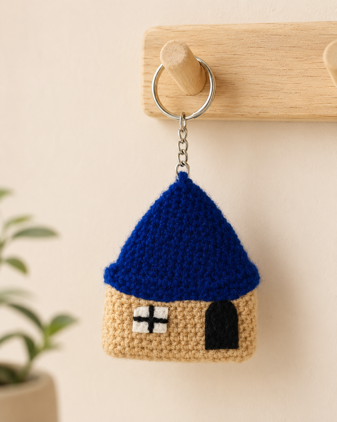 Crochet Blue Roof House Keychain hanging on a wooden wall hook, handmade house charm for keys and bags.