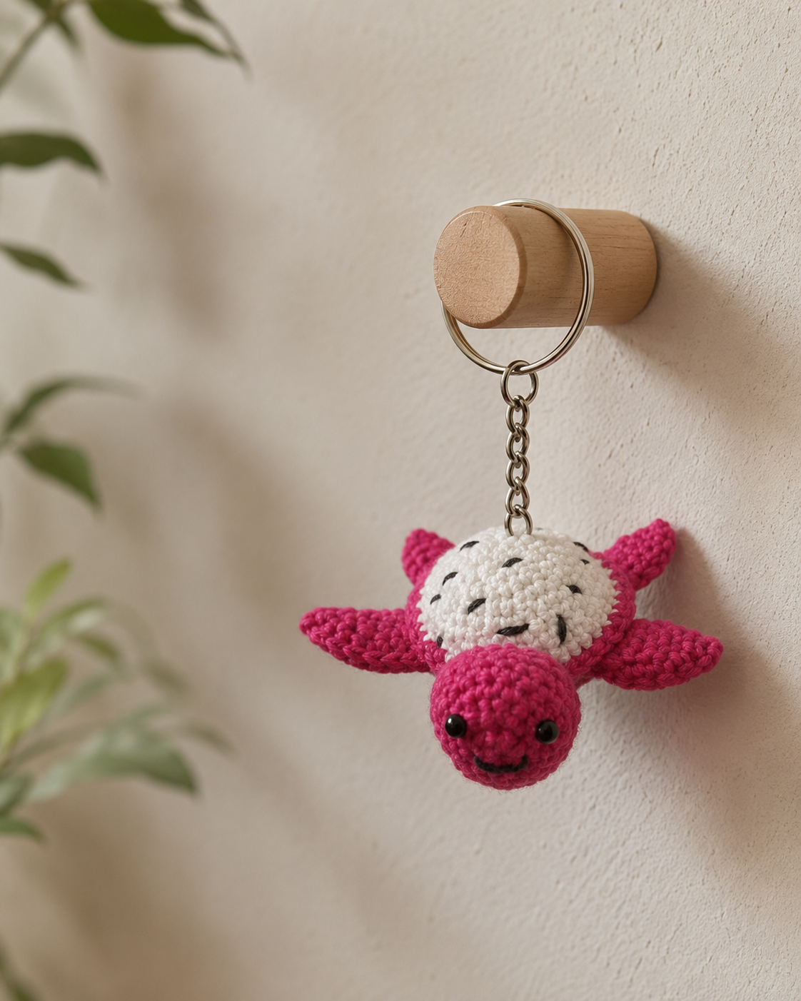 Blush turtle bag charm hanging on a wooden wall hook with a silver keyring and chain.