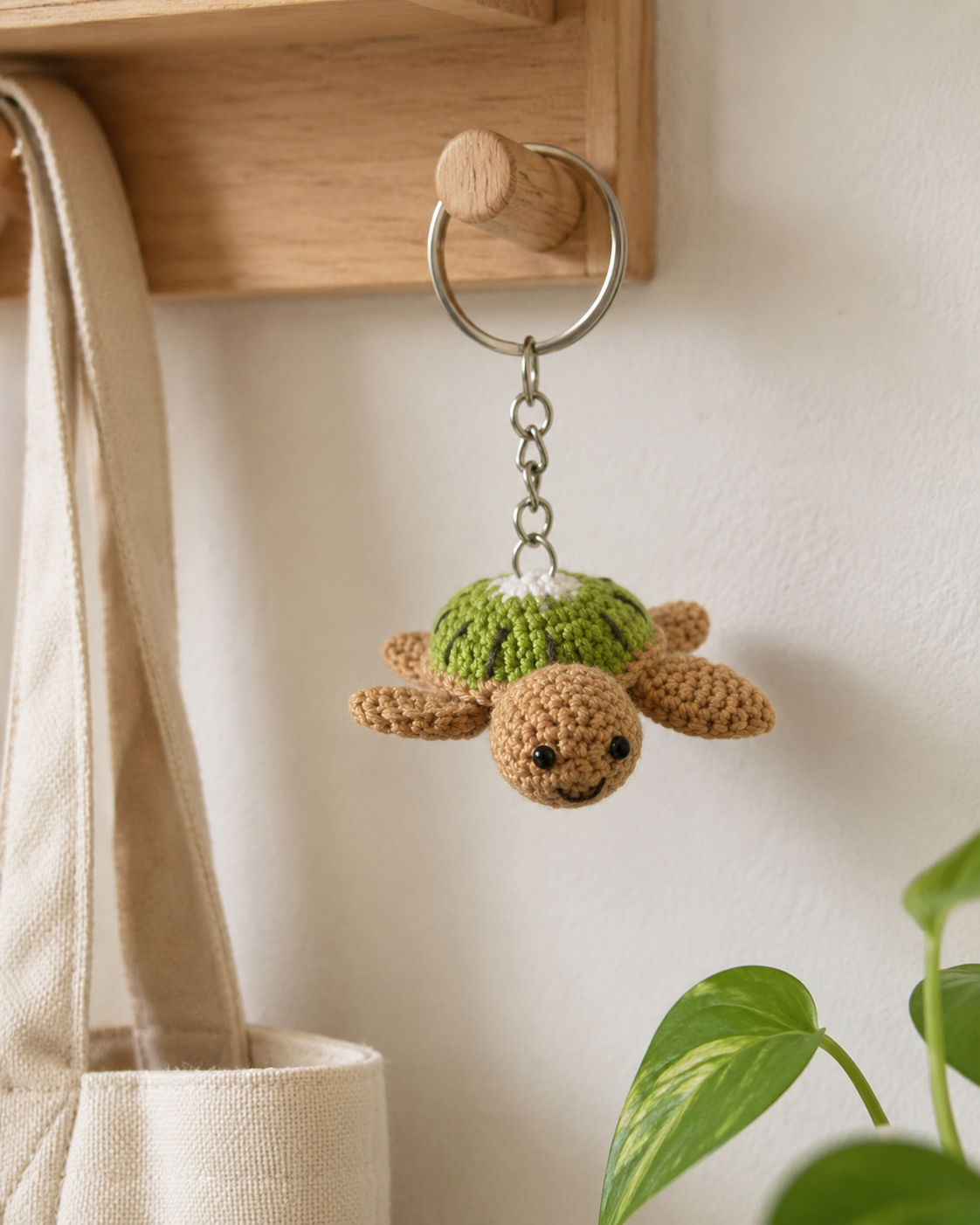 Green and tan turtle bag charm hanging from a wooden wall hook with silver keyring and chain.