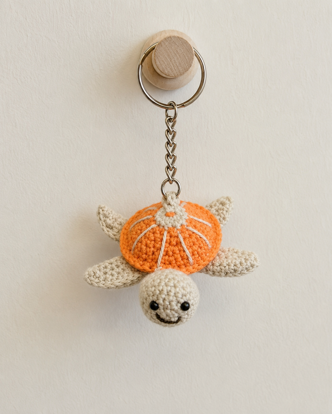 Orange cream turtle keychain hanging on a wooden wall hook, decorative turtle charm with metal ring and chain.