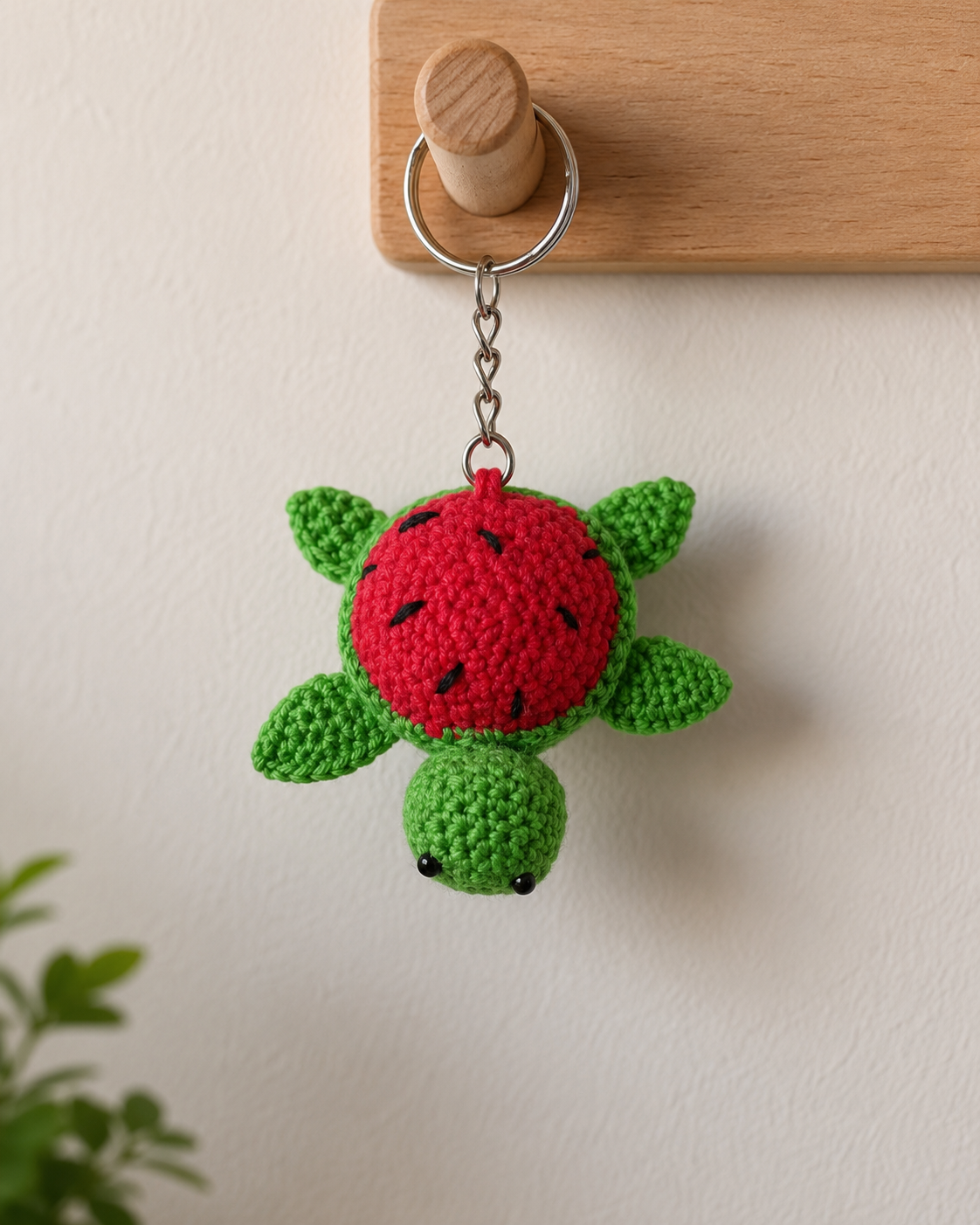 Watermelon shell turtle charm hanging on a wooden wall hook, cute green turtle keychain with red fruit-style shell.