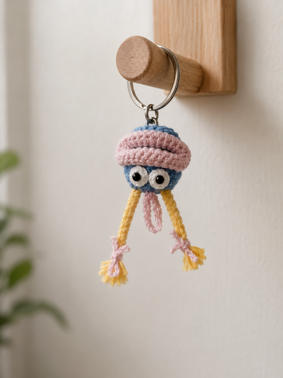 Pastel jelly charm hanging on a wooden wall hook, cute blue and pink handmade crochet keychain with yellow tassel legs.