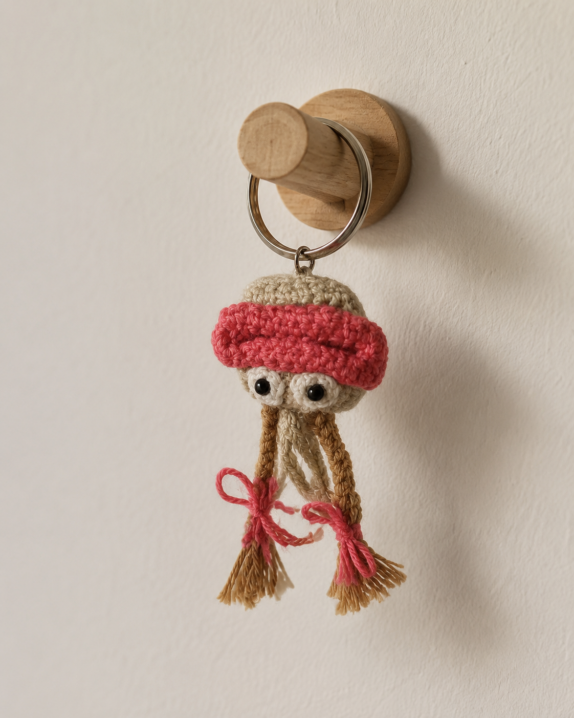 Blush jelly charm hanging on a wooden wall hook, pastel crochet sea creature keychain with pink and tan details.