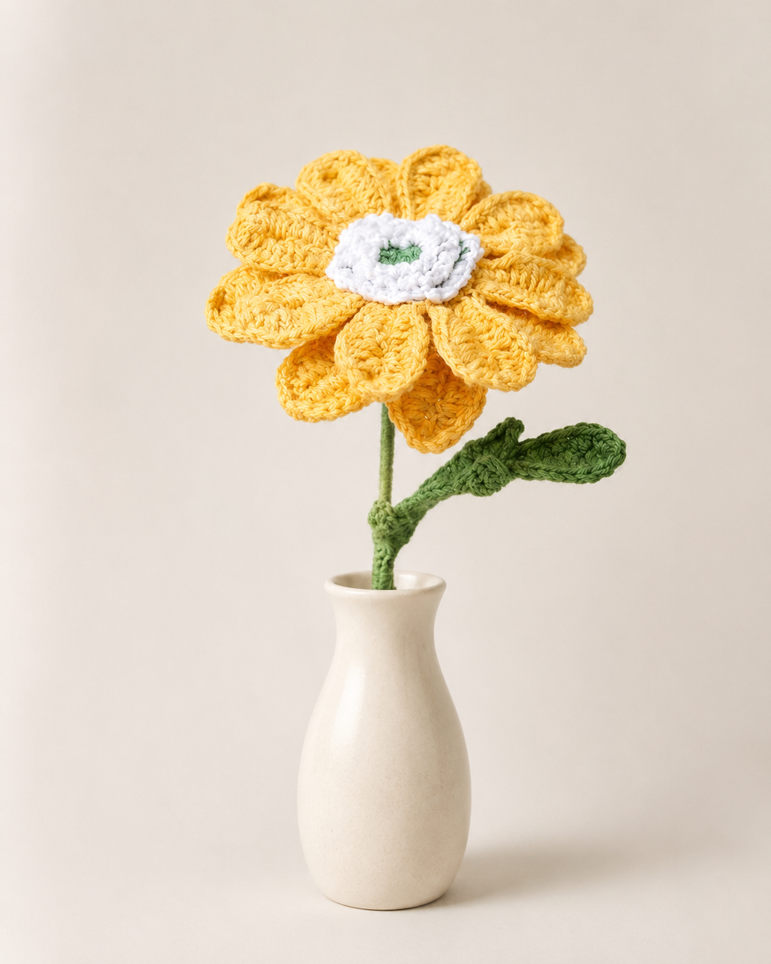 Golden yellow African daisy crochet flower stem displayed in a small cream vase on a neutral background.