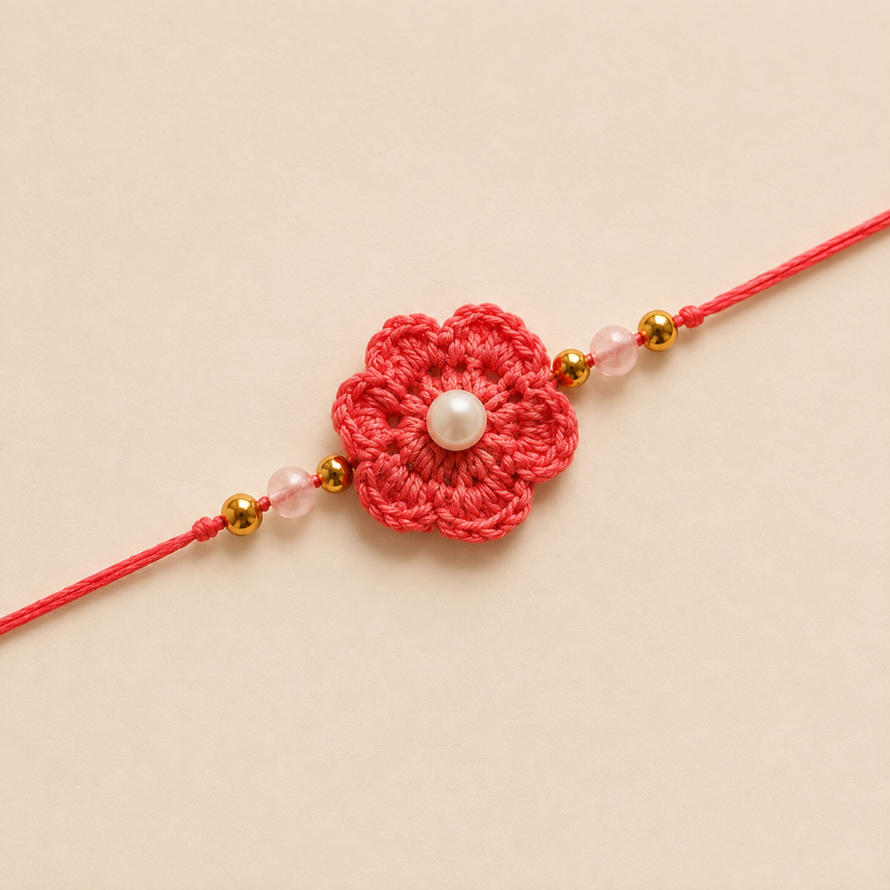 Close-up of coral floral rakhi with pearl-style center, gold-tone beads, soft pink beads, and coral tying thread.