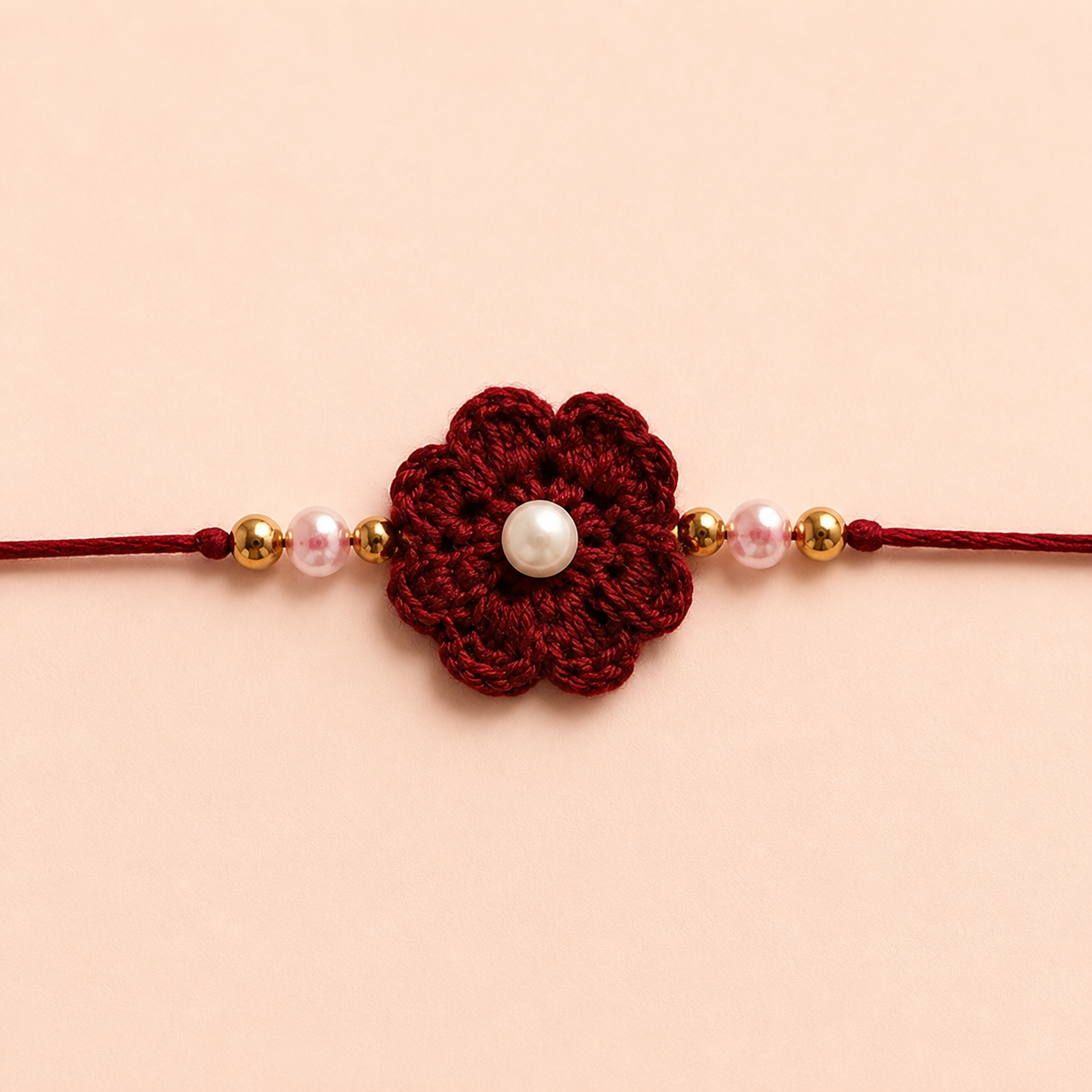 Close-up of ruby red flower rakhi with pearl-style center, gold-tone beads, soft pink pearl-like beads, and matching red thread.