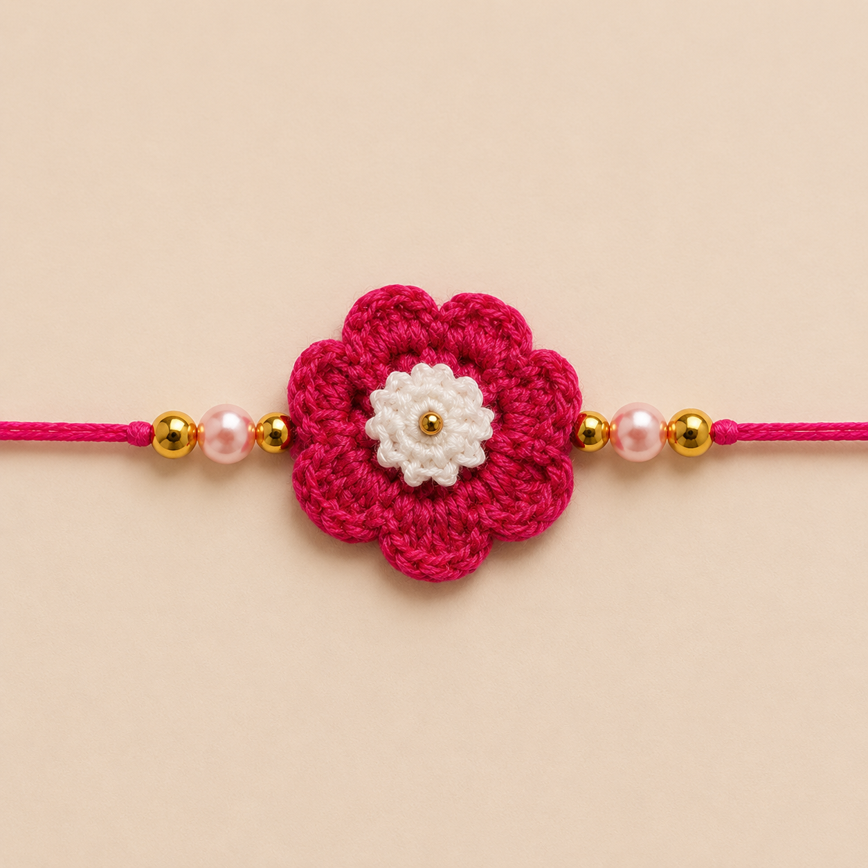 Close-up of hot pink flower rakhi with white center, gold bead detail, soft pink pearl beads, and gold-tone side beads.