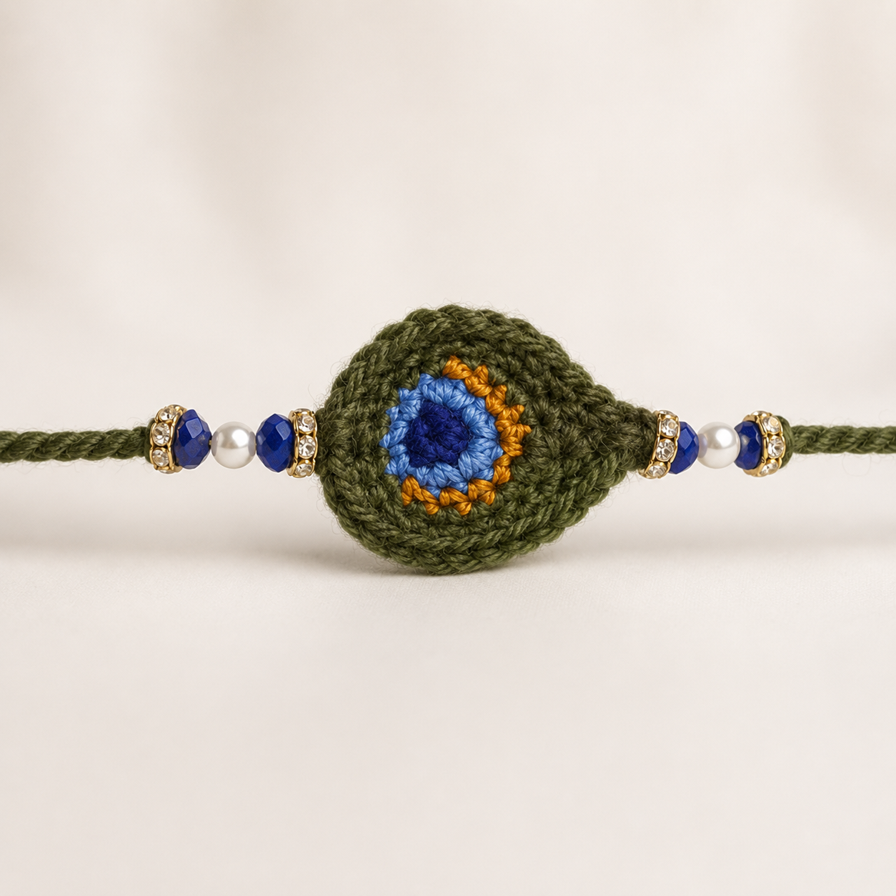 Close-up of Peacock Feather Rakhi centerpiece with green oval peacock-eye design, blue detailing, pearl beads, and gold-tone accents.