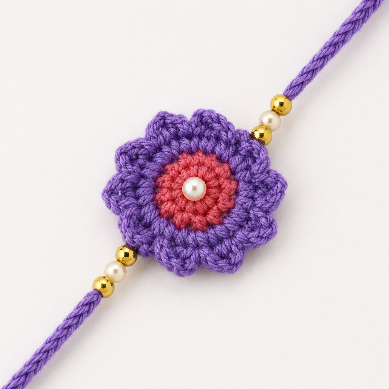 Close-up of purple flower rakhi with pink inner bloom, pearl-style center bead, gold beads, and purple thread, floral Raksha Bandhan rakhi for brother.