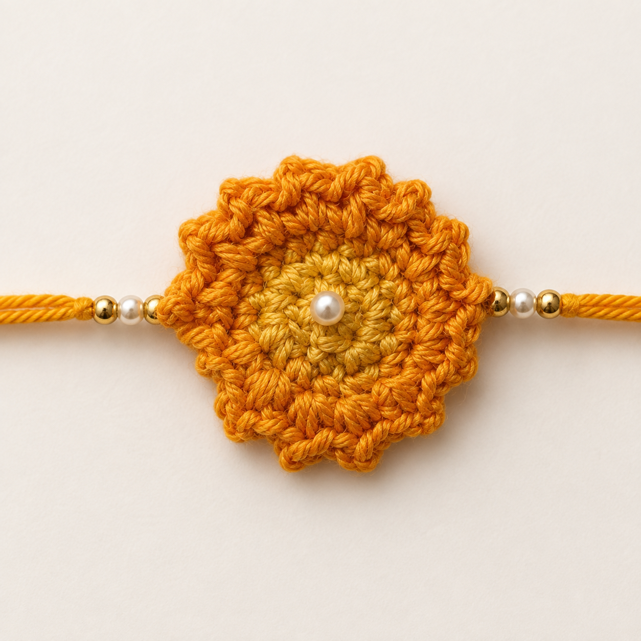 Close-up of Golden Sunflower Pearl Rakhi showing yellow and orange floral threadwork, pearl-style center bead, gold-tone side beads, and soft golden tying thread for Raksha Bandhan.