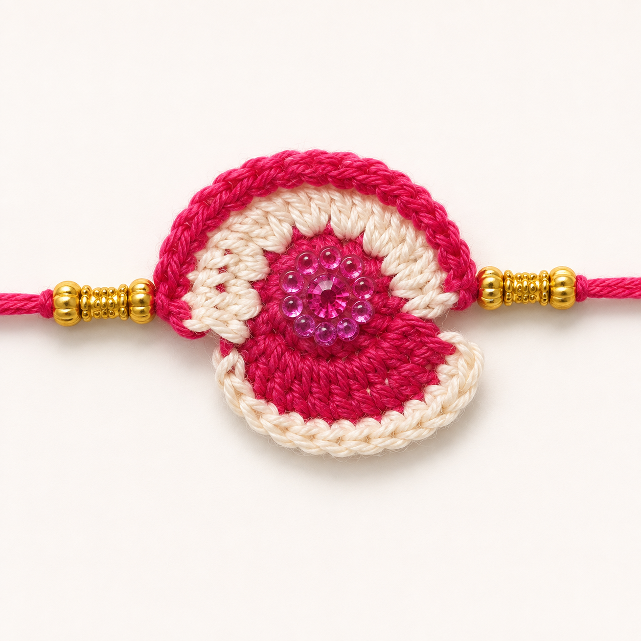 Close-up of Magenta Petal Shell Rakhi showing detailed yarn texture, cream and magenta shell-style motif, sparkling pink center embellishment, gold-tone beads, and festive thread rakhi design.
